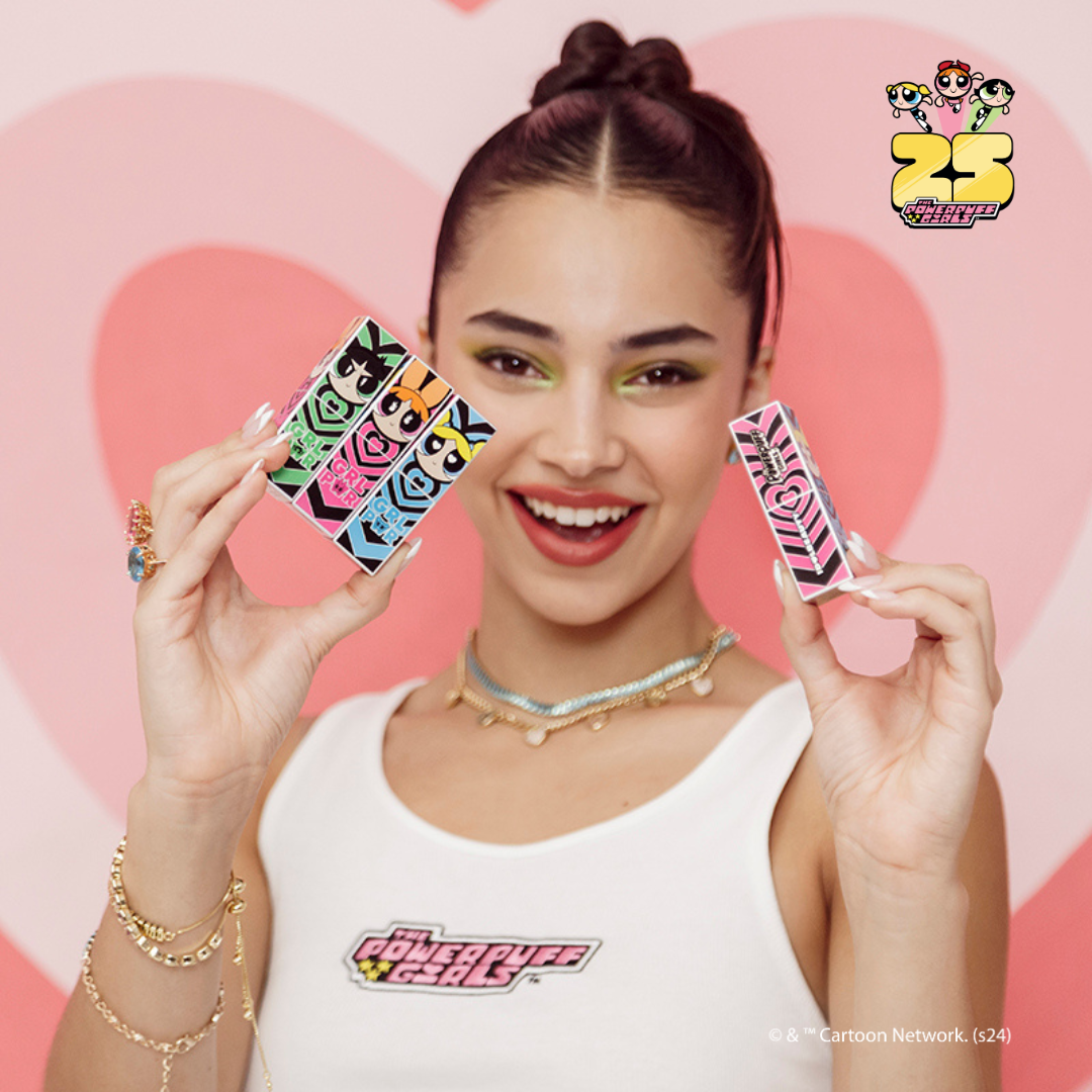 Una persona sostiene cajas de colores que representan personajes de dibujos animados sobre un fondo de corazón rosa, vistiendo una camiseta de Las Chicas Superpoderosas.