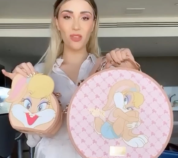 Una persona sostiene dos bolsas con temática de dibujos animados: una pequeña bolsa redonda con un personaje sonriente y una bolsa circular más grande con un diseño divertido.