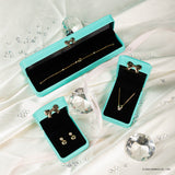 Elegantes joyas presentadas en cajas de terciopelo turquesa, que incluyen una pulsera, aretes y un collar, rodeados de diamantes falsos.